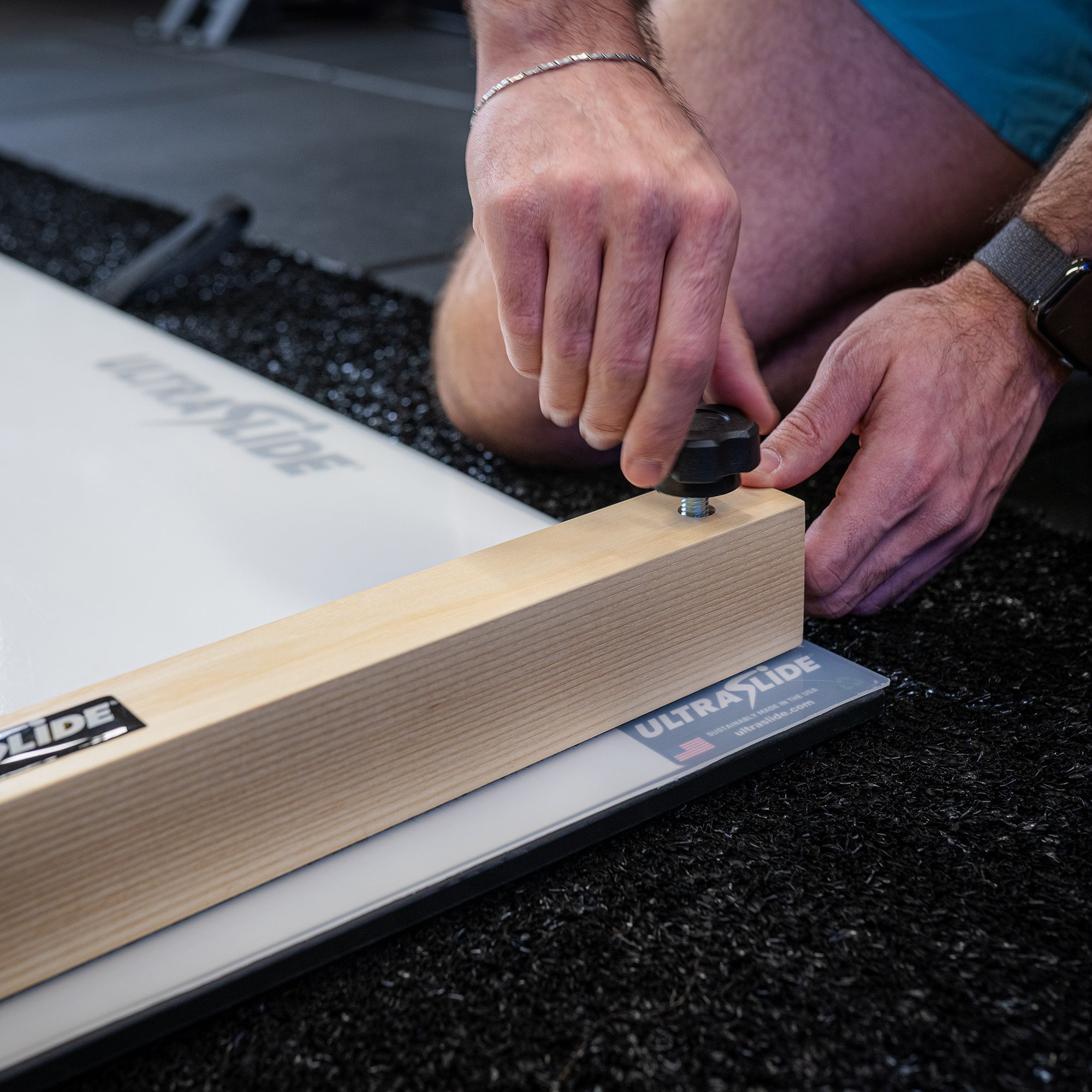 Person adjusting bumpers on an ULTRASLIDE slide board on a black textured surface