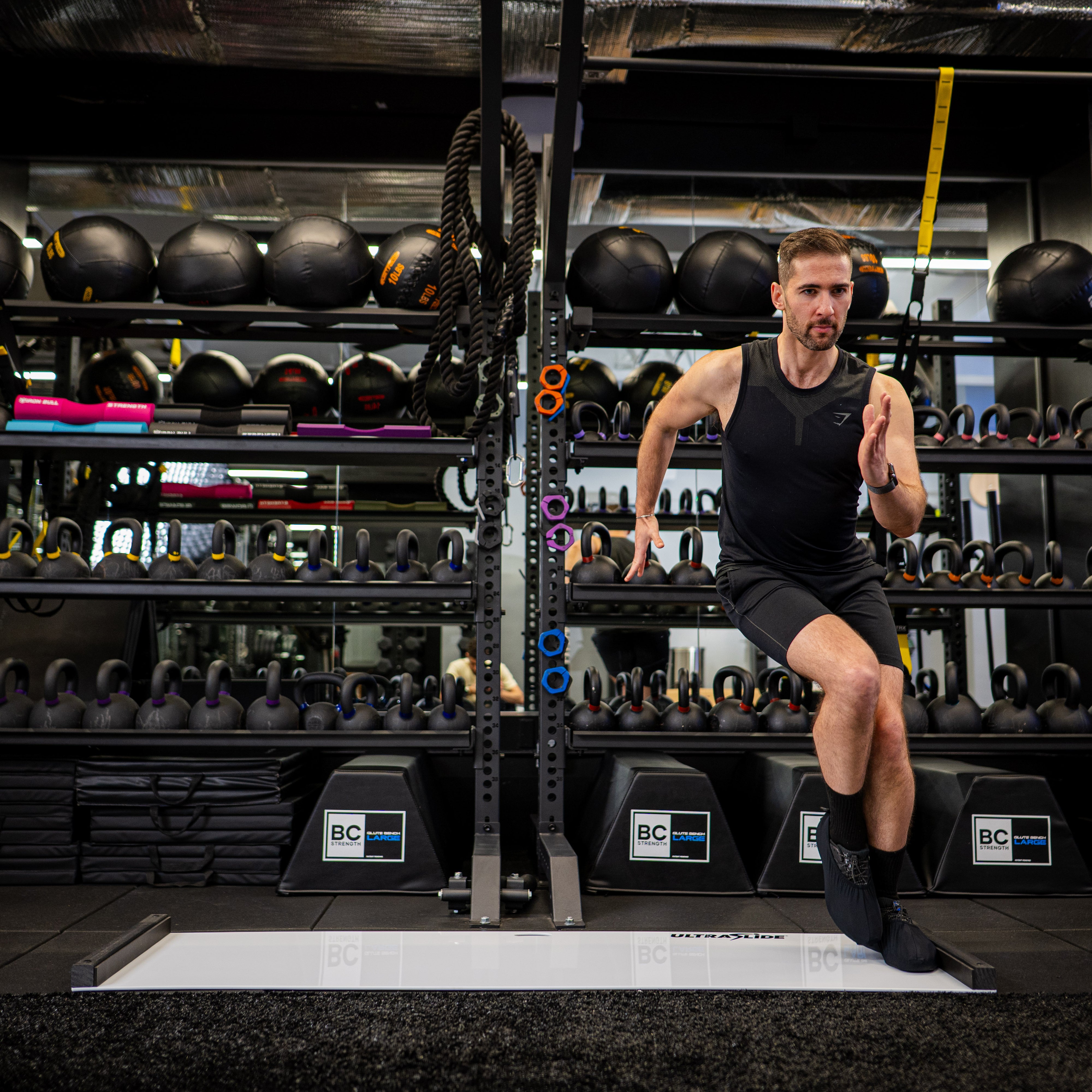 Man exercising on an ULTRASLIDE slide board in a gym with equipment and weights in the background