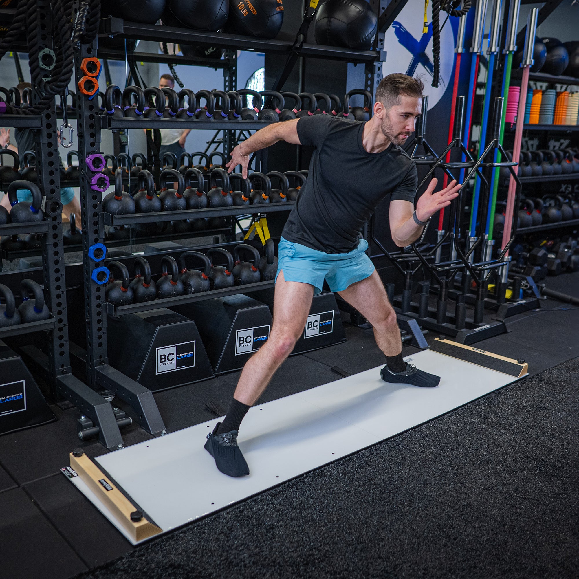 Man working out on an ULTRASLIDE slide board in a gym setting with various equipment in the background.