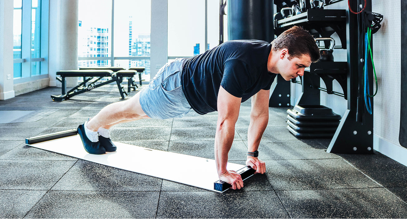 Man performing push-ups on an Ultraslide 6 slideboard in a gym setting