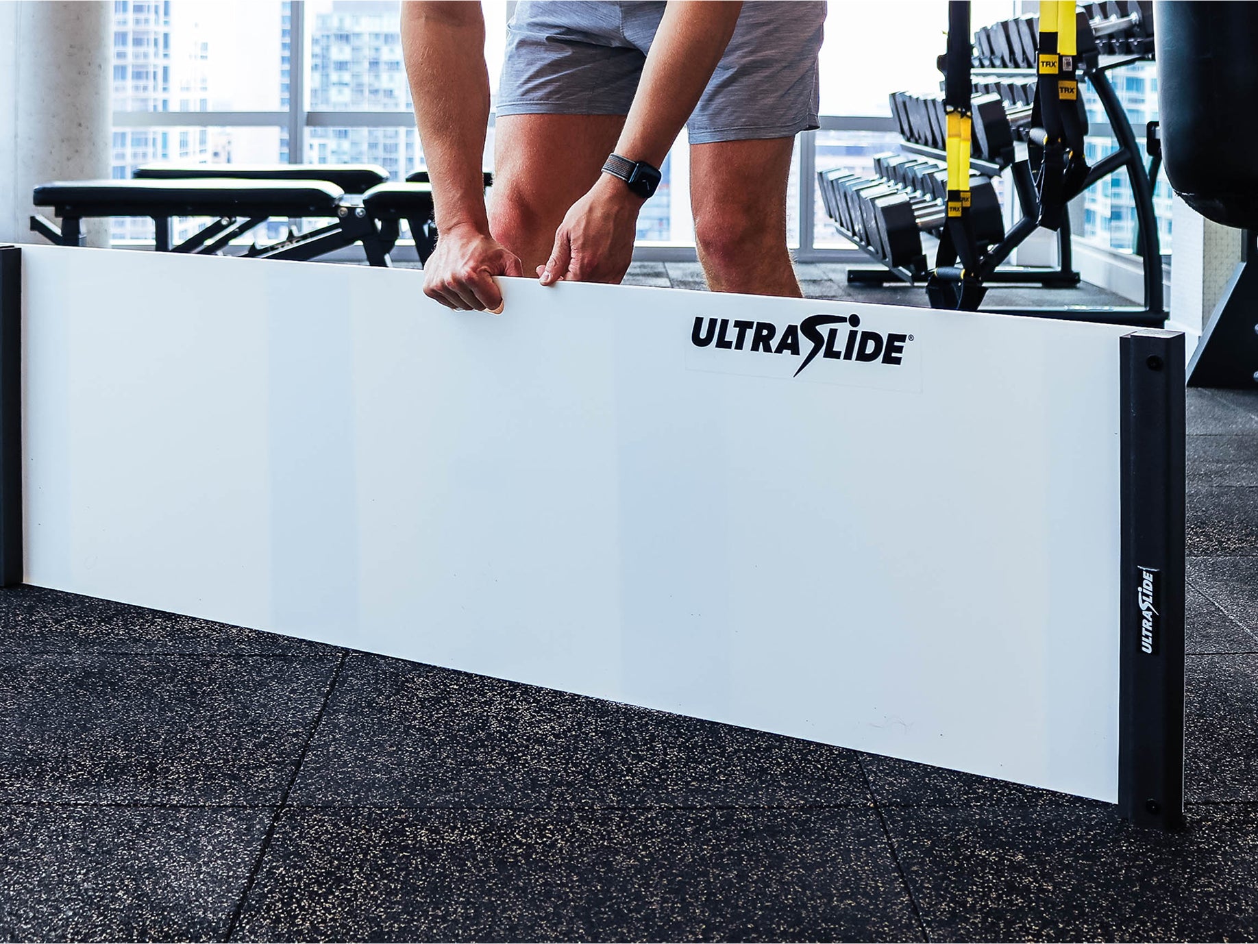 Person lifting a white UltraSlide 6 slideboard in a gym setting