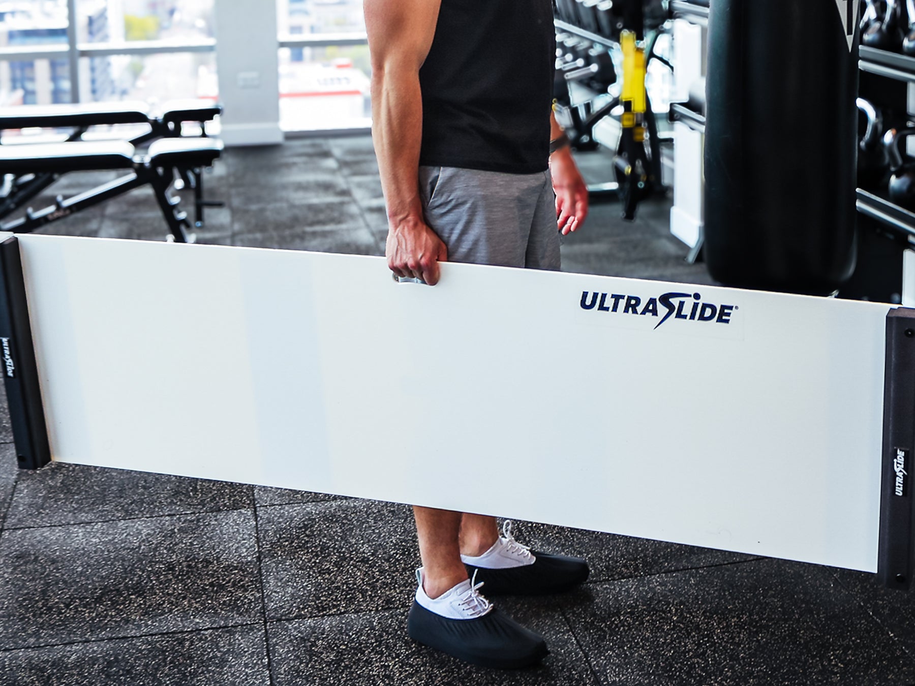 Person carrying a white UltraSlide 6 slideboard in a gym setting