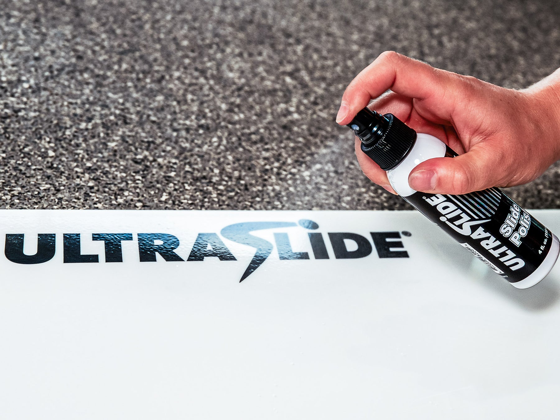 Hand holding a bottle of UltraSlide spray polish over an Ultraslide slideboard with the brand name visible.